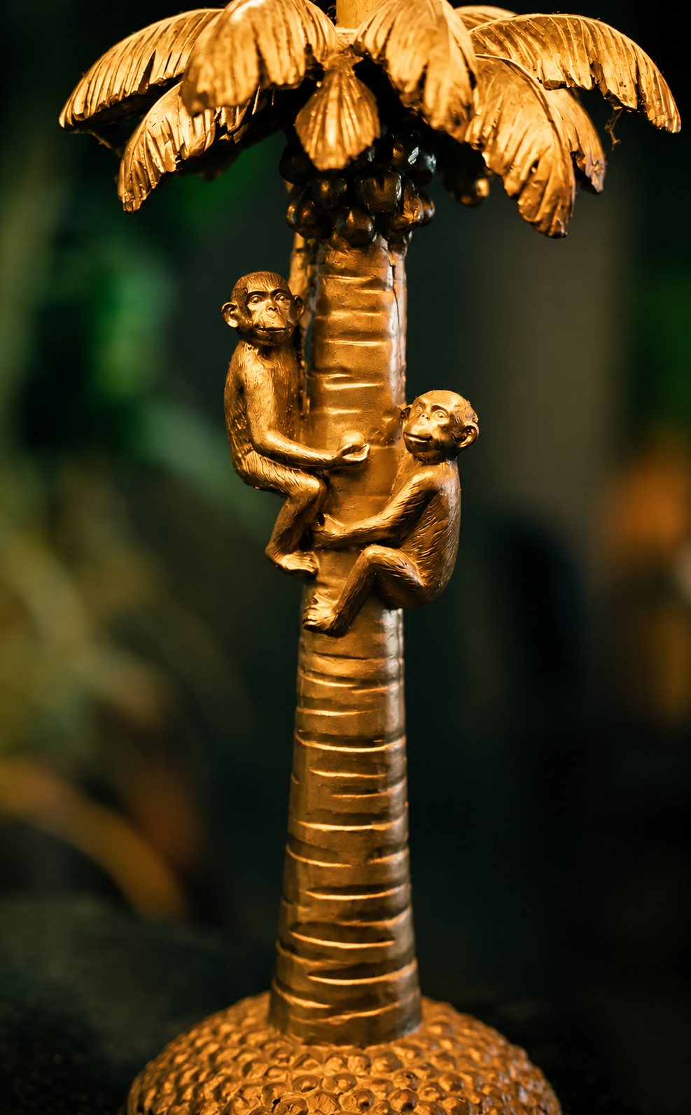 Objet décoratif doré représentant un palmier sur lequel grimpent deux petits singes, photographié devant un fond sombre et flou.