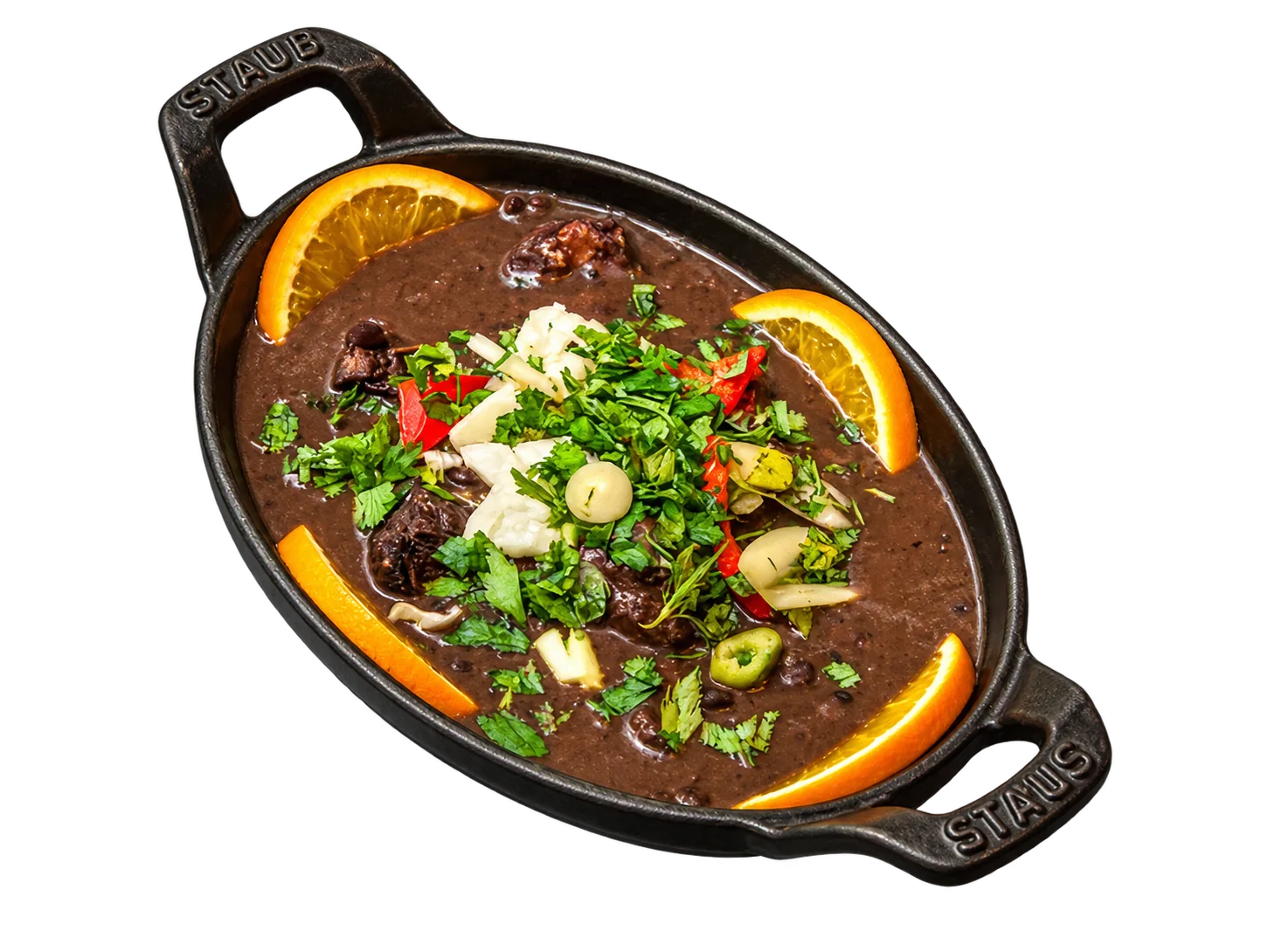 Un plat ovale en fonte noire contient une feijoada de haricots noirs garnie d'herbes fraîches, de piment rouge et de tranches d'orange.