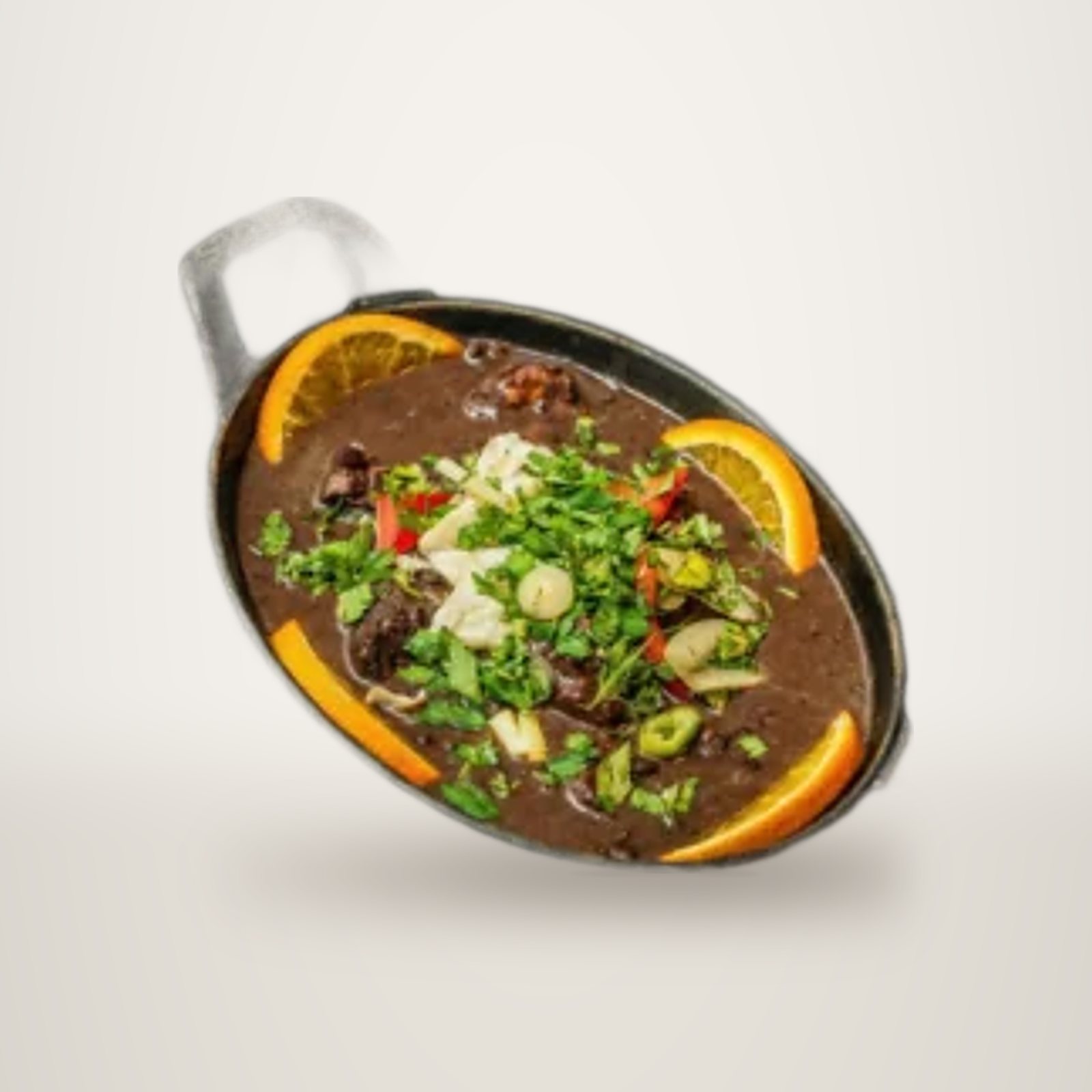 Un plat mijoté brun servi dans une petite cocotte en fonte noire, garni d'herbes ciselées, de poivron rouge et de tranches d'orange, posé sur une ardoise.