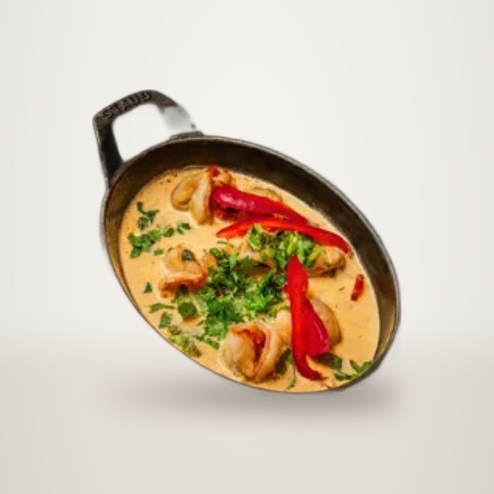 Une cocotte en fonte ovale posée sur une ardoise contient des morceaux de viande dans une sauce crémeuse, garnie de lanières de poivron rouge et d'herbes fraîches.